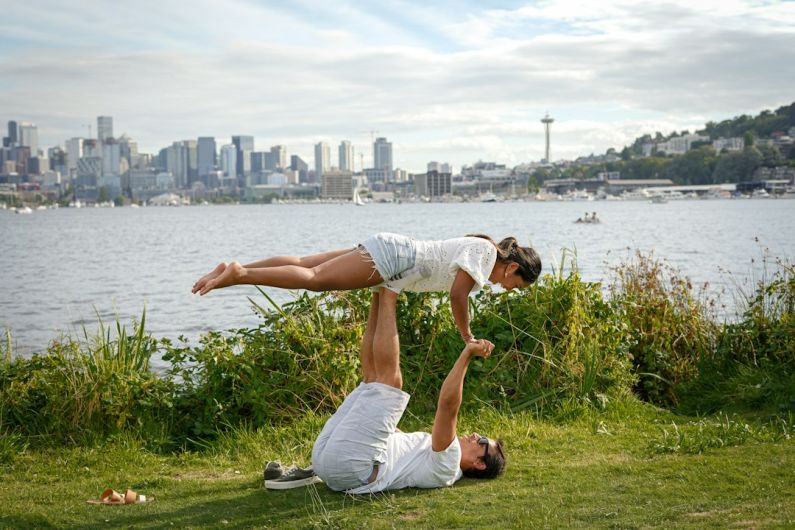 Partner Yoga - man in white t-shirt and white shorts sitting on green grass field near body of during